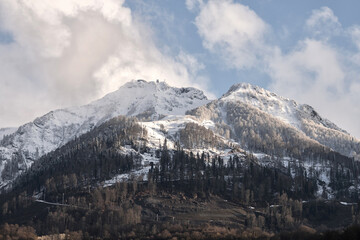 White clouds in blue sky moving over snowy white mountains during sunny day. Bright sunlight...