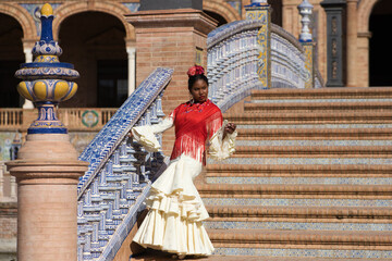 Young black woman dancing flamenco in a square in Seville, Spain. She wears a beige dress with...