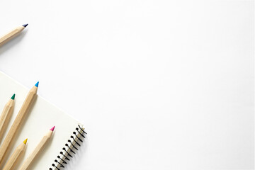Wooden pencils of different colors and a notebook on a white background.