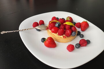cream cake with raspberries and blueberries and small macaroons served on a large white plate