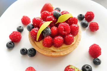 cream cake with raspberries and blueberries and small macaroons served on a large white plate