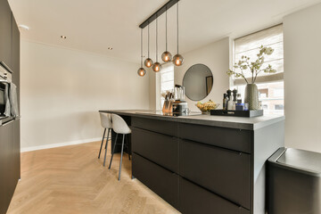 a kitchen and dining area in a modern home with wood flooring, white walls, black cabinetry and light fixtures