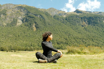 Fototapeta na wymiar A woman practice Yoga Pilates on the grass of the Milford Road valley with wind in her hair