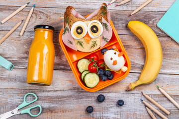 Funny owl sandwich with cheese and ham and egg in shape of rabbit. Orange juice in a glass bottle and a banana. School lunch box for kids. Top view. Copy space