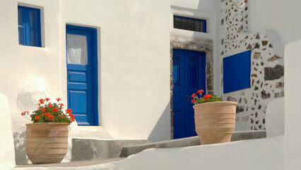 Cyclades traditional whitewashed house with blue doors, windows and flower pottery.