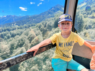 little child enjoying journey in cabin of funicular cable railway . Beautiful mountains on...