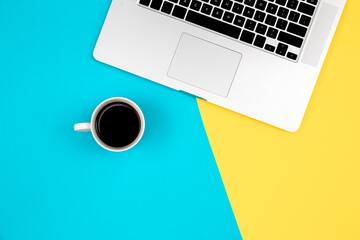 Laptop and cup of coffee on a yellow and blue background, flat lay.