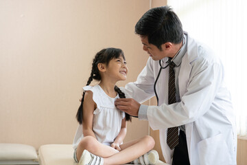 Doctor using stethoscope examining little girl patient at hospital. Medicine and health care concept.