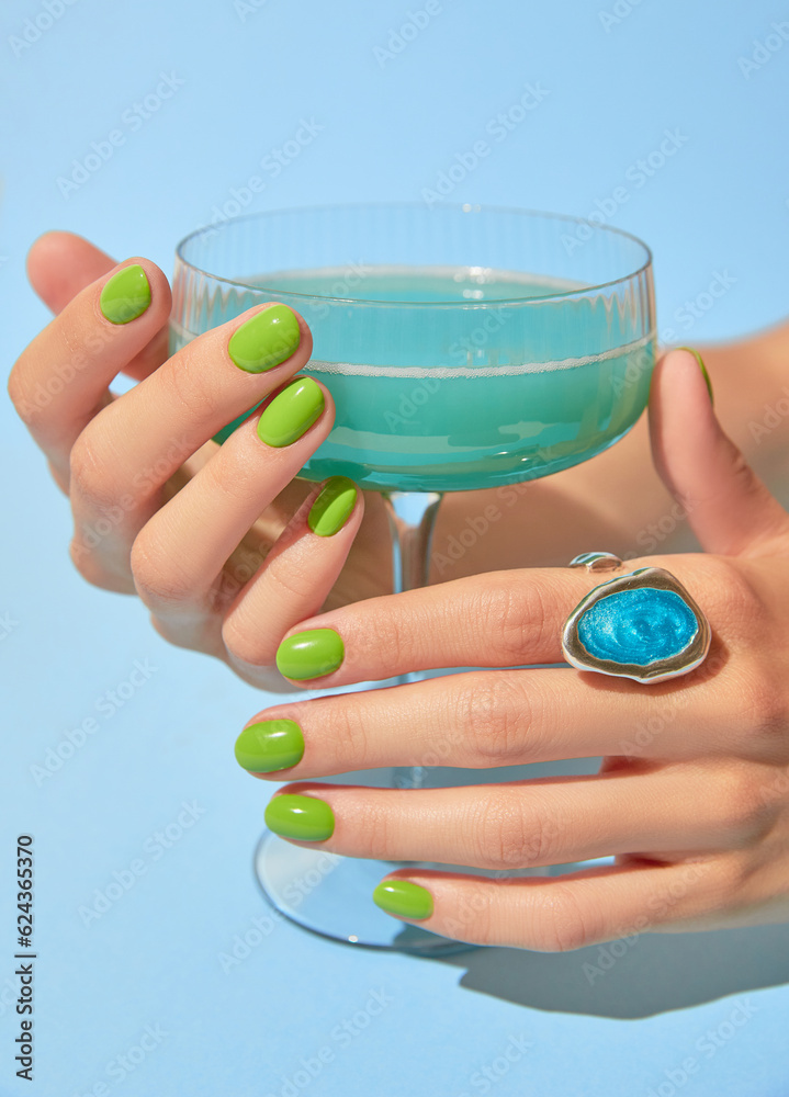 Wall mural beautiful womans hand with summer green nail design holding glass. manicure, pedicure beauty salon c