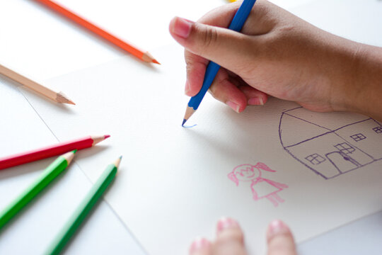 Close up children's hands draw and paint on white paper with colorful pencils.