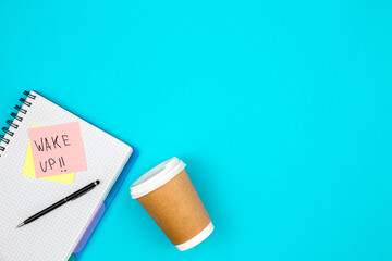 Paper cup and notebook with paper reminder with text Wake up, top view.