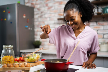 Young woman in kitchen. Beautiful African woman cooking pasta..