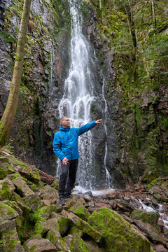 Tourist attraction of Germany - falls of Burgbach Waterfall near Schapbach, Black Forest, Baden-Wurttemberg, Germany. Man hiker in blue jacket standing on stone and looks at flow of falling water