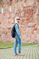 Fototapeta na wymiar Girl in sunglasses with a backpack in jeans clothes on the background of a brick building.