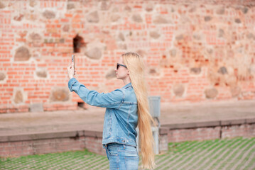 Obraz premium Blonde girl with long hair takes a photos or shoots a video on the smartphone.
