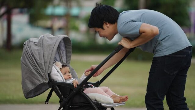 happy father talking and playing with his infant baby in the stroller while resting in the park