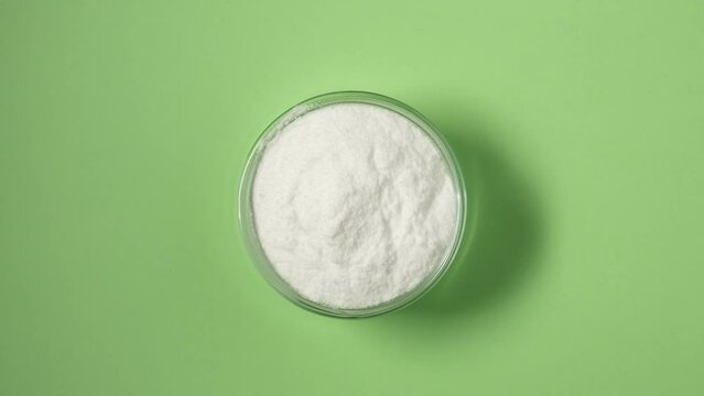 Dextrose monohydrate powder, d-Glucose or Grape sugar in glass bowl on green background, top view. Natural sweetener, sugar substitute. Video 4K, Rotating.