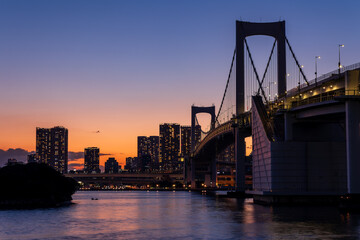 Fototapeta na wymiar Purple and orange sky during sunset behind the skyscrapers of Tokyo and the Rainbow Bridge in Tokyo Bay