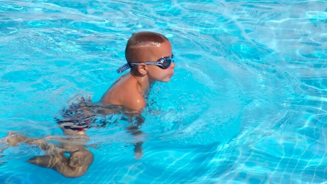 Little boy in swimming goggles swimming under water in a pool.