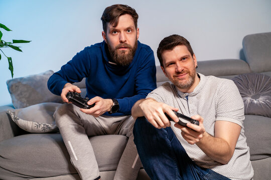 Two male best friends playing video games with joypad at home, night time