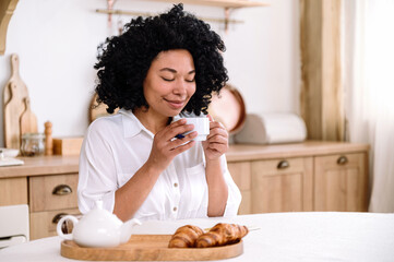Smiling african american woman sitting in kitchen and drinking coffee