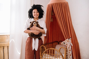 Woman standing near woven cradle and holding teddy bear © brizmaker