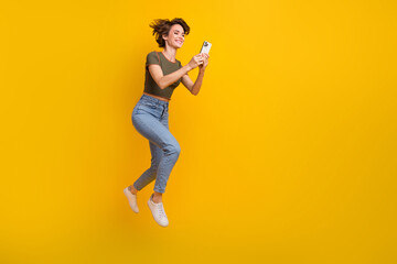 Fototapeta na wymiar Full length photo of excited funky girl dressed top jumping texting twitter telegram facebook empty space isolated yellow color background