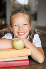 Primary schoolgirl, in school uniform, with a book and apple.