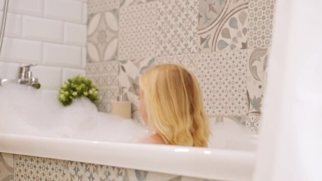 Cute funny caucasian blonde three years old girl taking bath with white foam bubbles, playing,smiling , having fun.Carefree childhood, kid body care concept. 