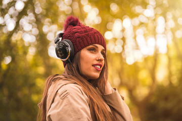 Portrait of a woman in autumn in a forest with brown leaves listening to music with headphones