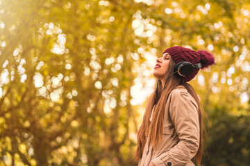 Portrait of a woman in autumn in a forest with brown leaves with her eyes closed listening to music...