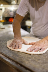 Pizzaiolo napoletano mentre stende con le mani un disco di pizza sul banco da lavoro in marmo pronto per essere condito e infornato