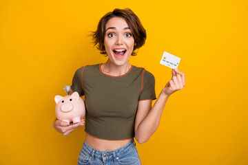 Photo of excited funny girl dressed khaki top collecting money piggy box rising credit card...