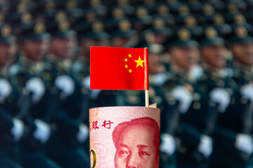 A roll of Chinese bank notes and national flag with a military background. A Chinese arms spending,...