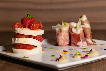 Piatto d'antipasto di un ristorante con millefoglie di mozzarella con pomodori e involtini di prosciutto crudo ripieni di ricotta