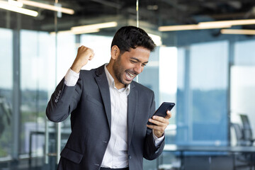 Young arab businessman happy celebrating victory reading news online, man got win holding joyfully...