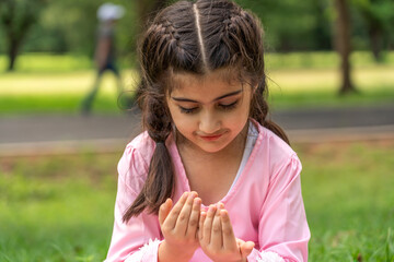Portrait of happy religious asian islam muslim kid, girl pray to god with hijab dress, Hari Raya day, Eid al-Fitr, fasting, islam, ramadan in summer park