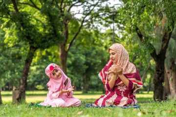 Portrait of happy religious happy love asian islam family muslim mother teaching muslim girls child pray to god with hijab dress, Hari Raya day, Eid al-Fitr, fasting, islam, ramadan in summer park