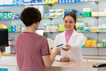Customer gives a health insurance card to a young pharmacist inside the pharmacy