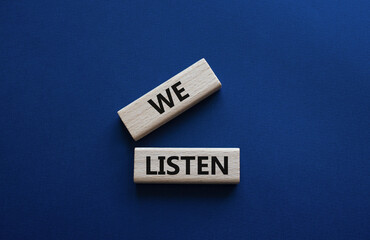 We listen symbol. Wooden blocks with words We listen. Beautiful deep blue background. Business and We listen concept. Copy space.