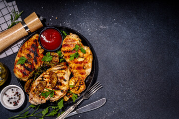 Grilled roasted chicken, turkey fillet. Spicy bbq fried white meat boneless fillet with garlic, rosemary, lemon and ketchup sauce, on black concrete table background top view copy space