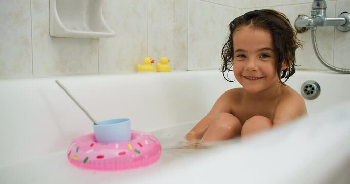 A girl bathes in a bathtub with toys. Smiling happy child is washing himself under water. High quality 4k footage