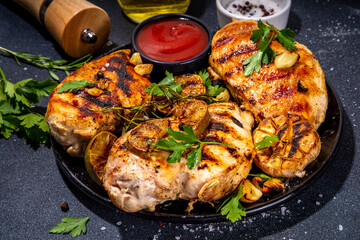Grilled roasted chicken, turkey fillet. Spicy bbq fried white meat boneless fillet with garlic, rosemary, lemon and ketchup sauce, on black concrete table background top view copy space