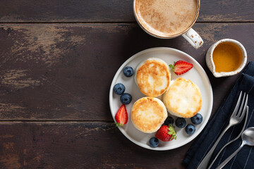 Syrniki with berries, honey and coffee cappuccino on a wooden table. Cottage cheese pancakes. Sweet breakfast or lunch meal, top view, copy space