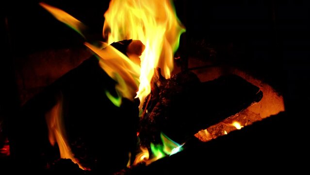 Close up of burning wood in fire pit at night and emitting greenish flames from it as if some chemicals or plastic is burn. Actually there is special natural compound or powder mix used to make colors