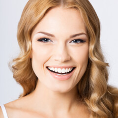 Face portrait photo of beautiful young cheerful smiling woman, over gray background. Happy amased attractive blond girl at studio. Dental health concept.