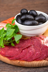 Close-up of sliced pastrami, black olives and green basil.