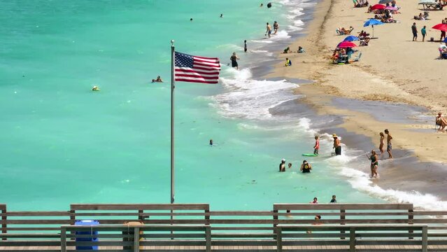 Aerial view of American national flag waving at Venice fishing pier in Florida, USA. Many people enjoing vacation time swimming in gulf water and relaxing