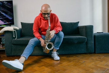 latin man musician at home sitting with his saxophone looking down thinking about a piece of music