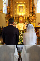 A young couple stands in front of the altar during a wedding ceremony in a Catholic church.